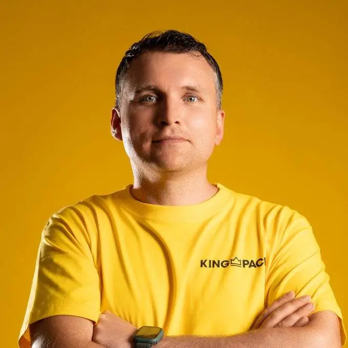 Mann im gelben KingPac-T-Shirt vor gelbem Hintergrund, verschränkte Arme; Porträt, einheitliches Farbschema.